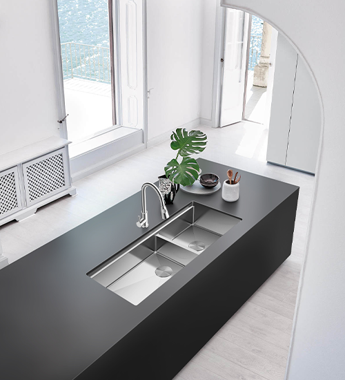 Minimalist black kitchen island with rectangular stainless steel sink, silver faucet, bright windows, white walls, and small plant decoration