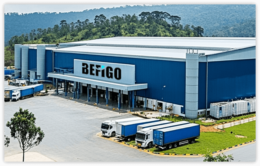 A modern factory building with a blue-green facade, multiple floors with windows, air conditioning units, and a glass entrance area. The building has a professional industrial appearance.