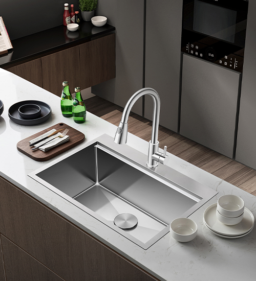 Modern kitchen with rectangular stainless steel sink embedded in white countertop with wooden cabinets below, silver faucet, and kitchen items including plates and bottles